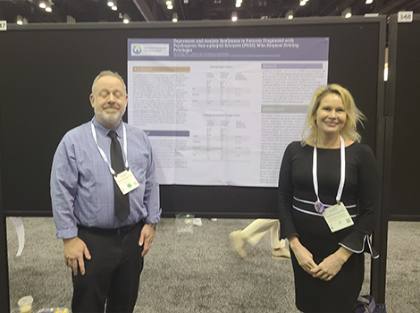 Dr's. Trobliger and Kramska posing next to poster on PNES 